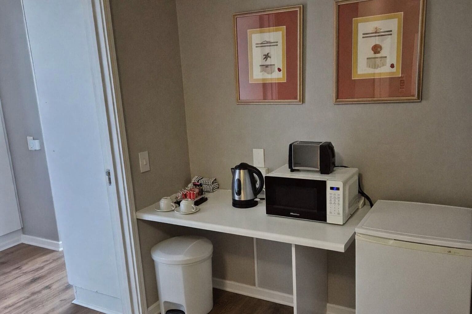 A small kitchenette with a microwave, toaster, kettle, and a trash bin.
