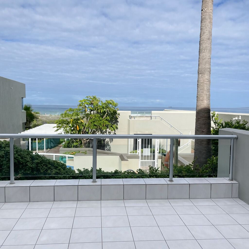 A balcony with a view of the ocean, a palm tree, and a modern building.