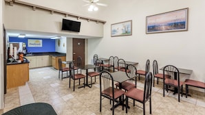 A dining area with multiple tables and chairs, a kitchen area with a blue counter, and a television mounted on the wall. - Days Inn by Wyndham Yuma (Yuma)