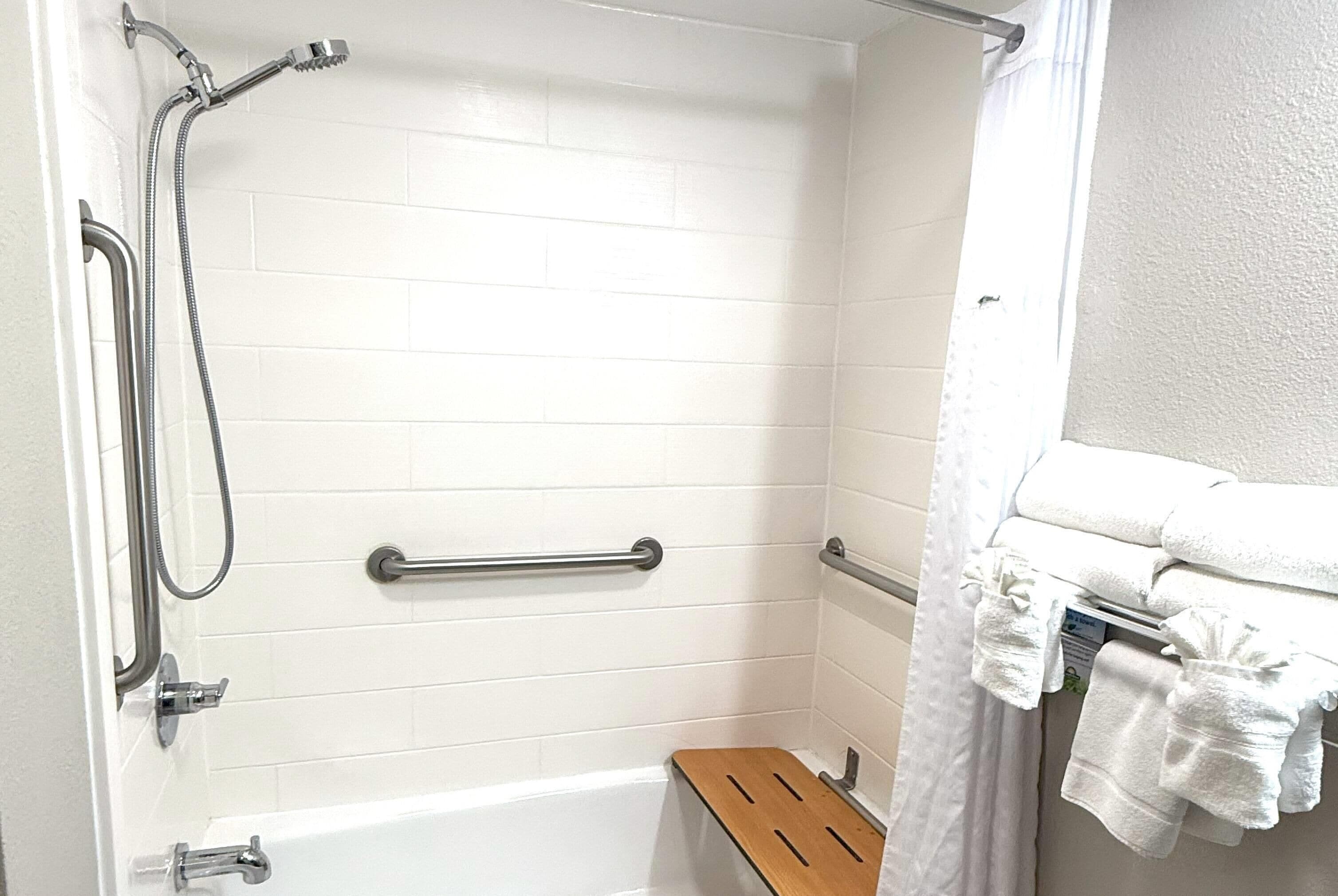 A shower area with a grab bar, a bench, and a towel rack.