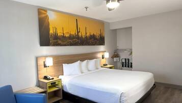 Habitación de hotel con una cama grande, ventilador de techo, mesita de noche con teléfono, escritorio con lámpara y perchero en la pared.