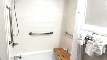 A bathroom with a white bathtub, grab bars, a wooden bath tray, a towel rack, and a black countertop.