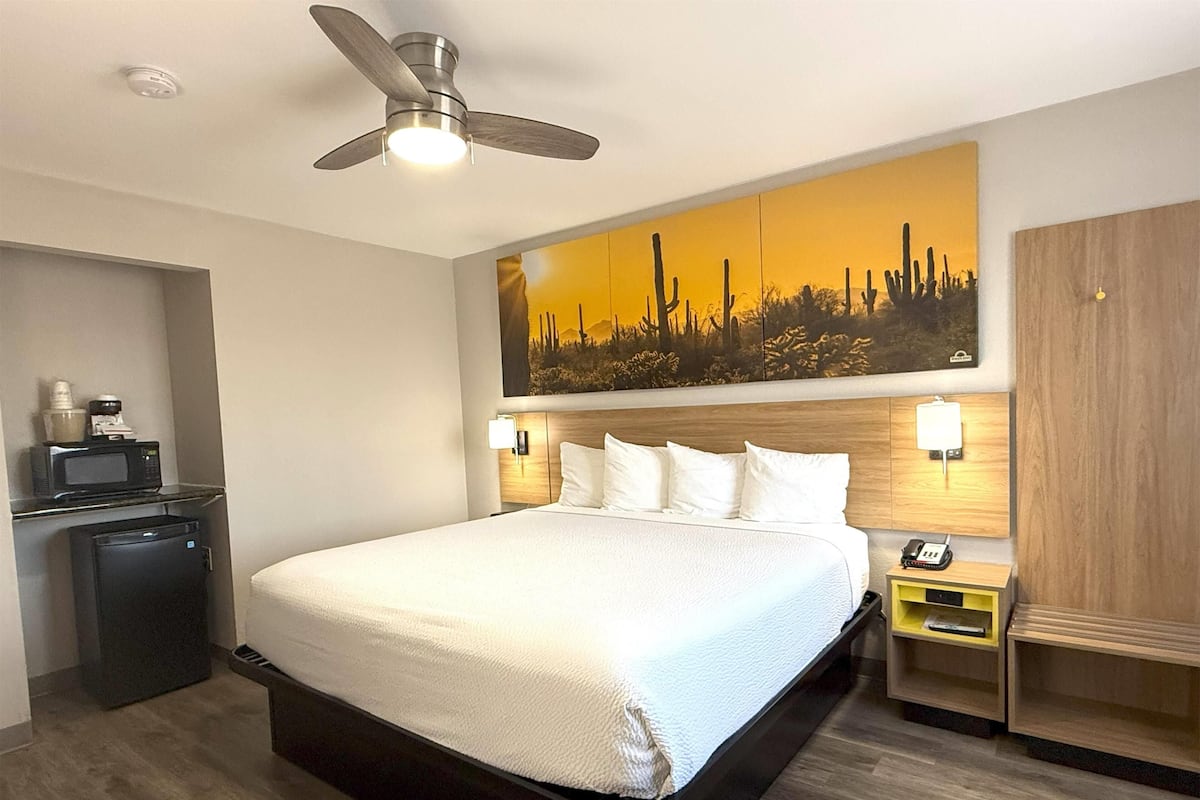 Une chambre d’hôtel équipée d’un lit, d’un ventilateur de plafond, d’un four à micro-ondes, d’un mini-réfrigérateur, d’une table de chevet et d’une armoire en bois.