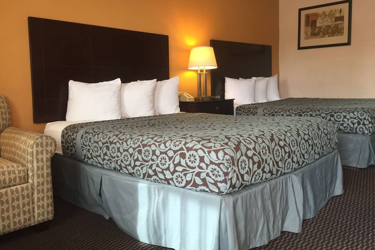 Une chambre d’hôtel avec deux lits, une table de chevet, une lampe, une chaise et un tableau encadré au mur.