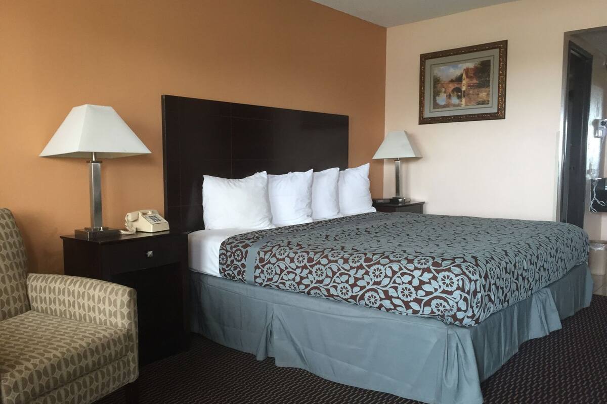 A hotel room with a bed, two bedside tables, a chair, a painting on the wall, and a door.