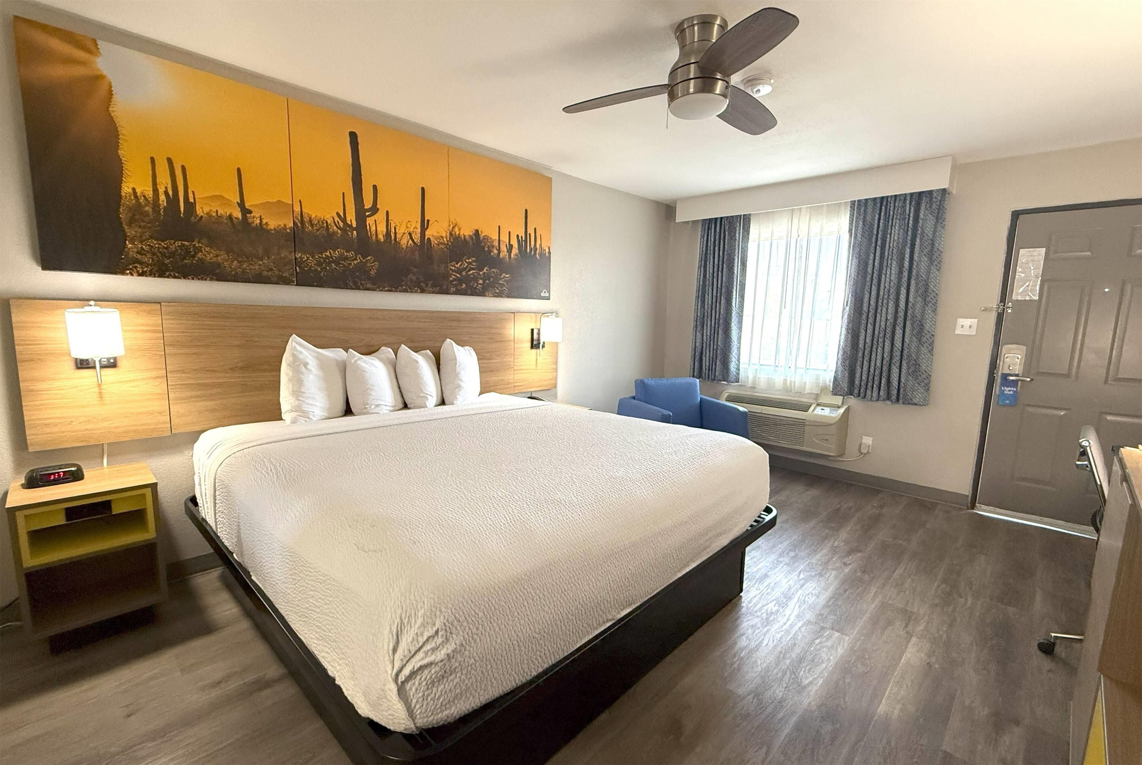 Habitación de hotel con una cama grande, ventilador de techo, aire acondicionado de pared y un ventanal con cortinas.