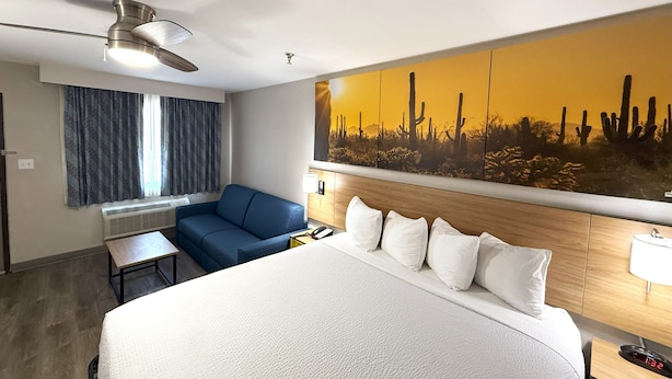 A hotel room with a large bed, a blue sofa, a desk, and a wall-mounted TV. - Days Inn by Wyndham Yuma (Yuma)