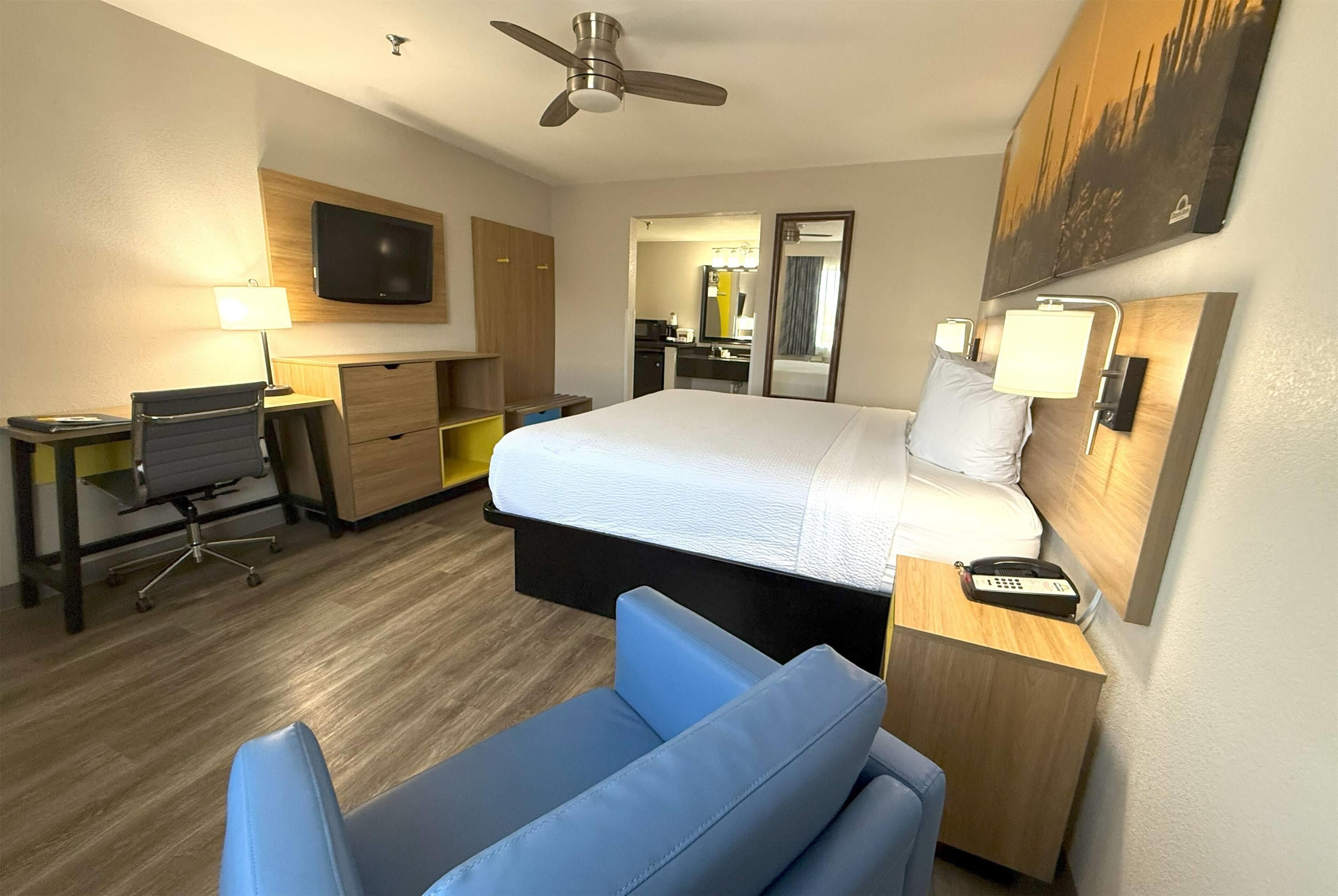 Een hotelkamer met een bed, bureau, stoel en een plafondventilator.