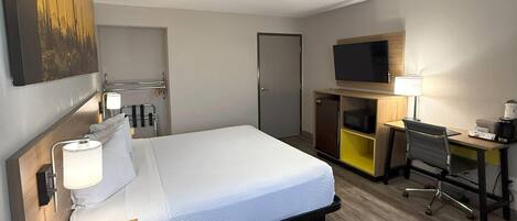 A hotel room with a bed, desk, chair, TV, ceiling fan, and a painting on the wall.