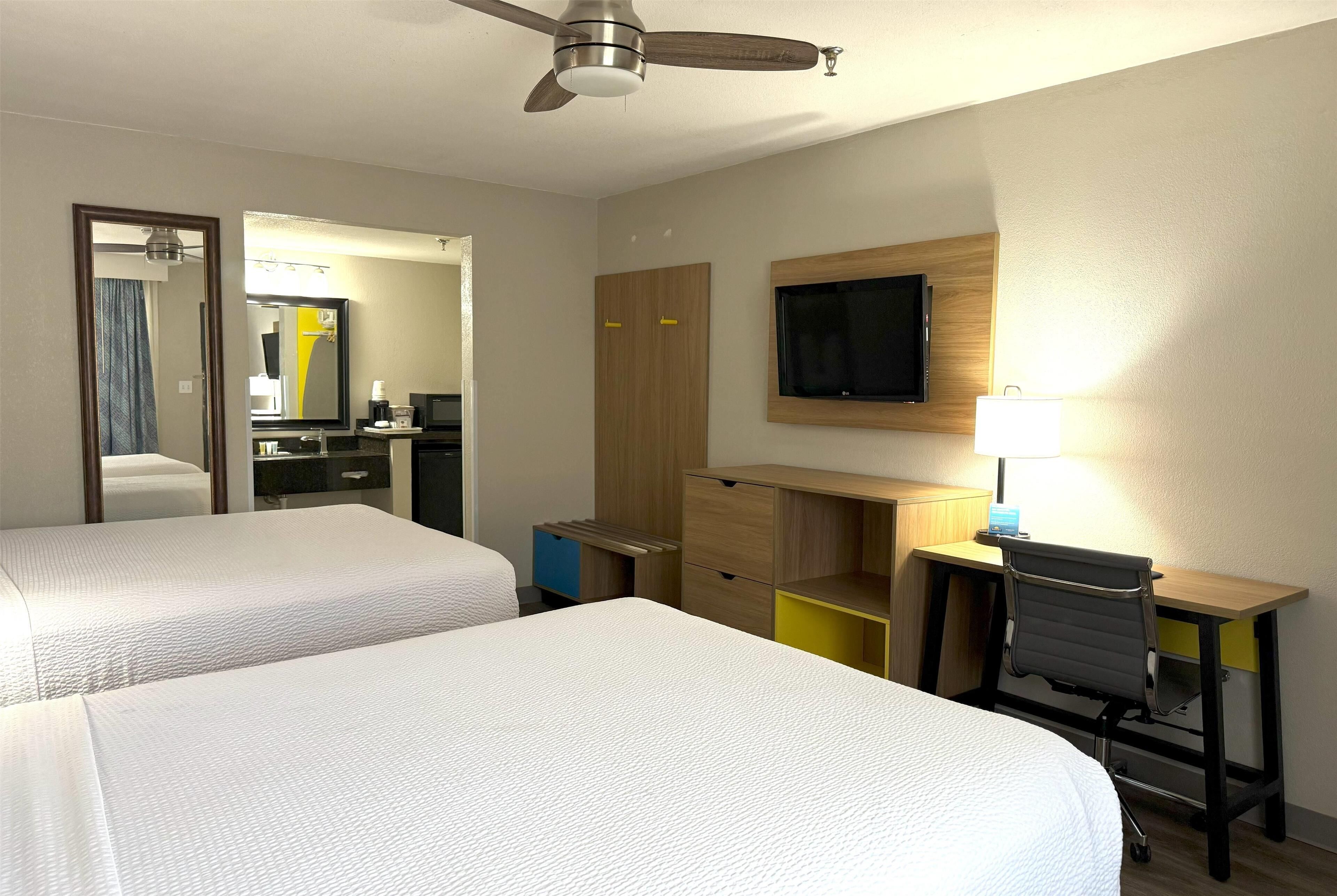 A hotel room with two beds, a desk with a chair, a television, and a ceiling fan.