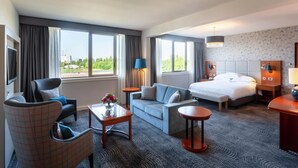A hotel room with a large bed, a sofa, a chair, a small table, and a TV.