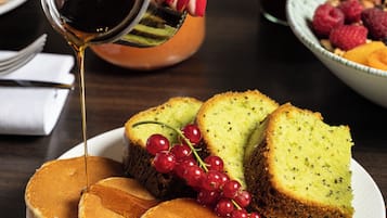 A plate with pancakes, cake, and red currants, with syrup being poured over them.