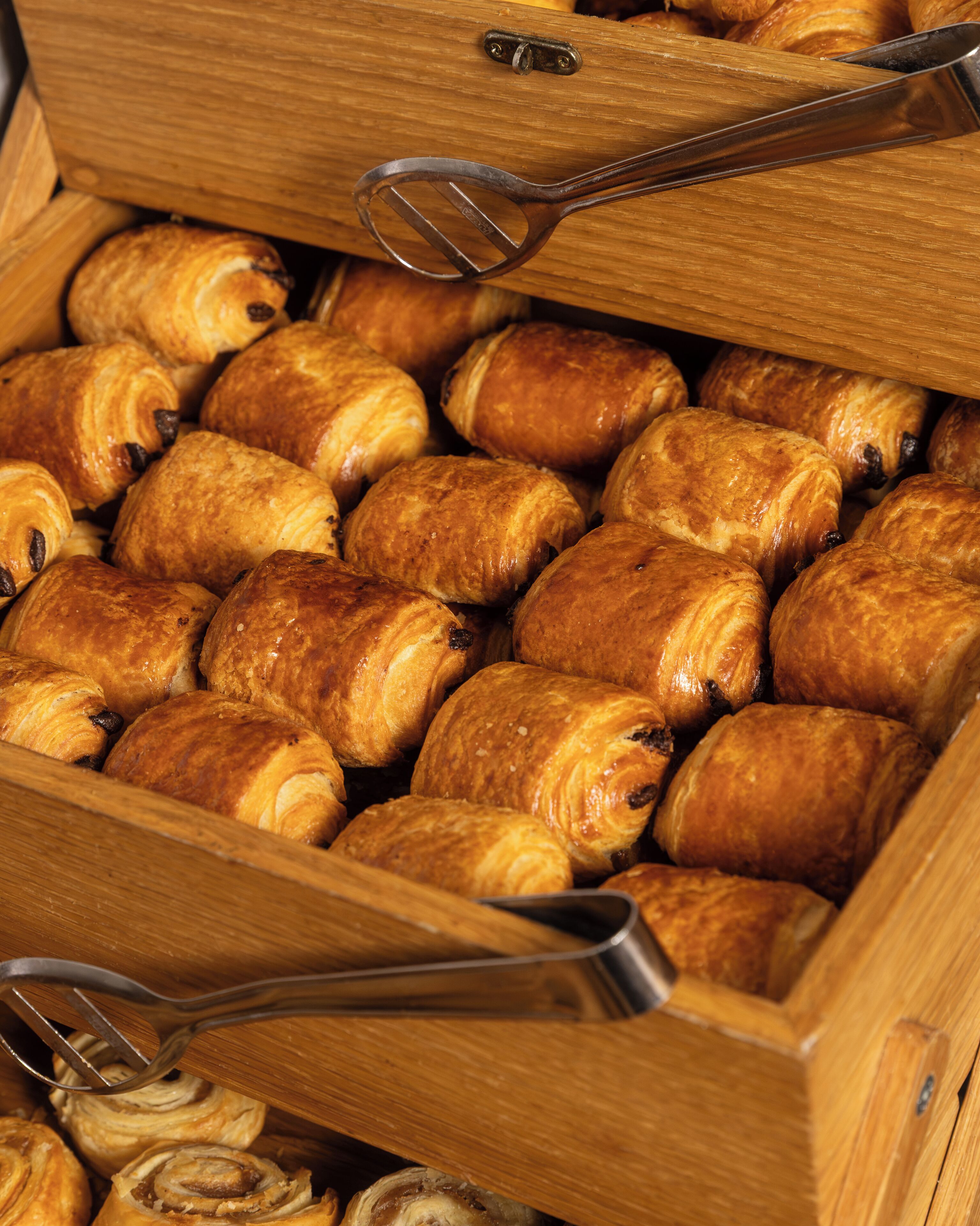 En trækasse fyldt med forskellige bagværk, blandt andet croissanter og rundstykker.