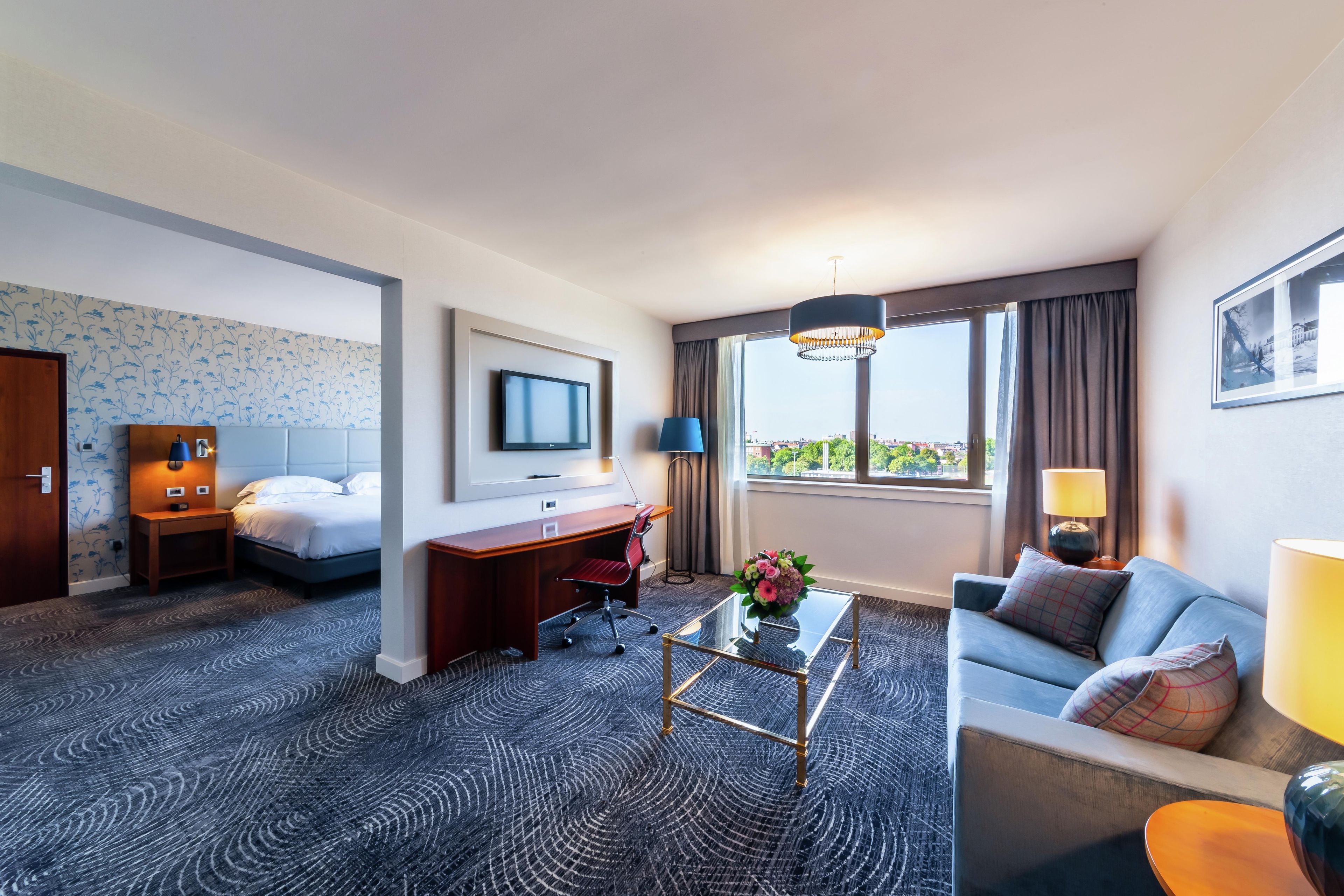 A hotel room with a bed, desk, sofa, and a large window with a view.