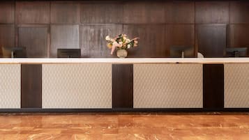 A reception desk with a vase of flowers, wooden paneling, and a marble floor.