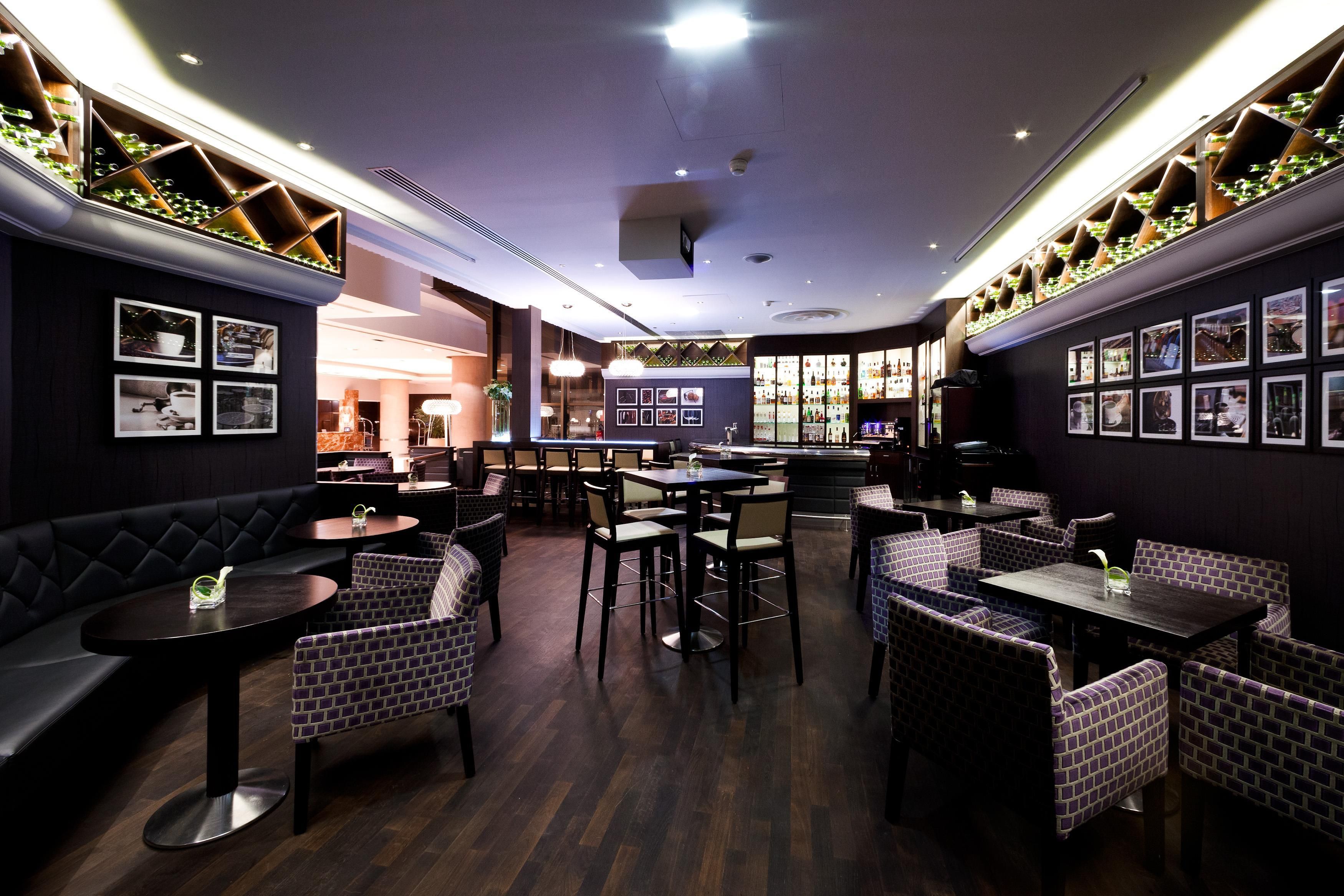 Interior de restaurante con suelo de madera oscura, asientos con motivo de ladrillo y una zona de bar con una estantería para vinos.