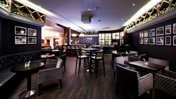 A restaurant with dark wood flooring, cushioned seating, and a central dining area with tables and chairs.