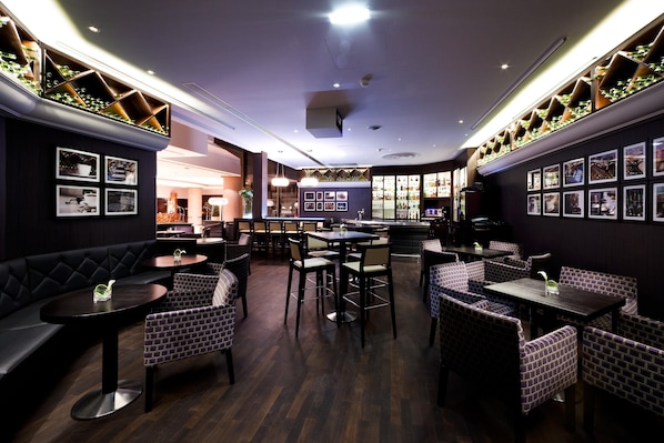 A restaurant with dark wood flooring, cushioned seating, and a central dining area with tables and chairs.