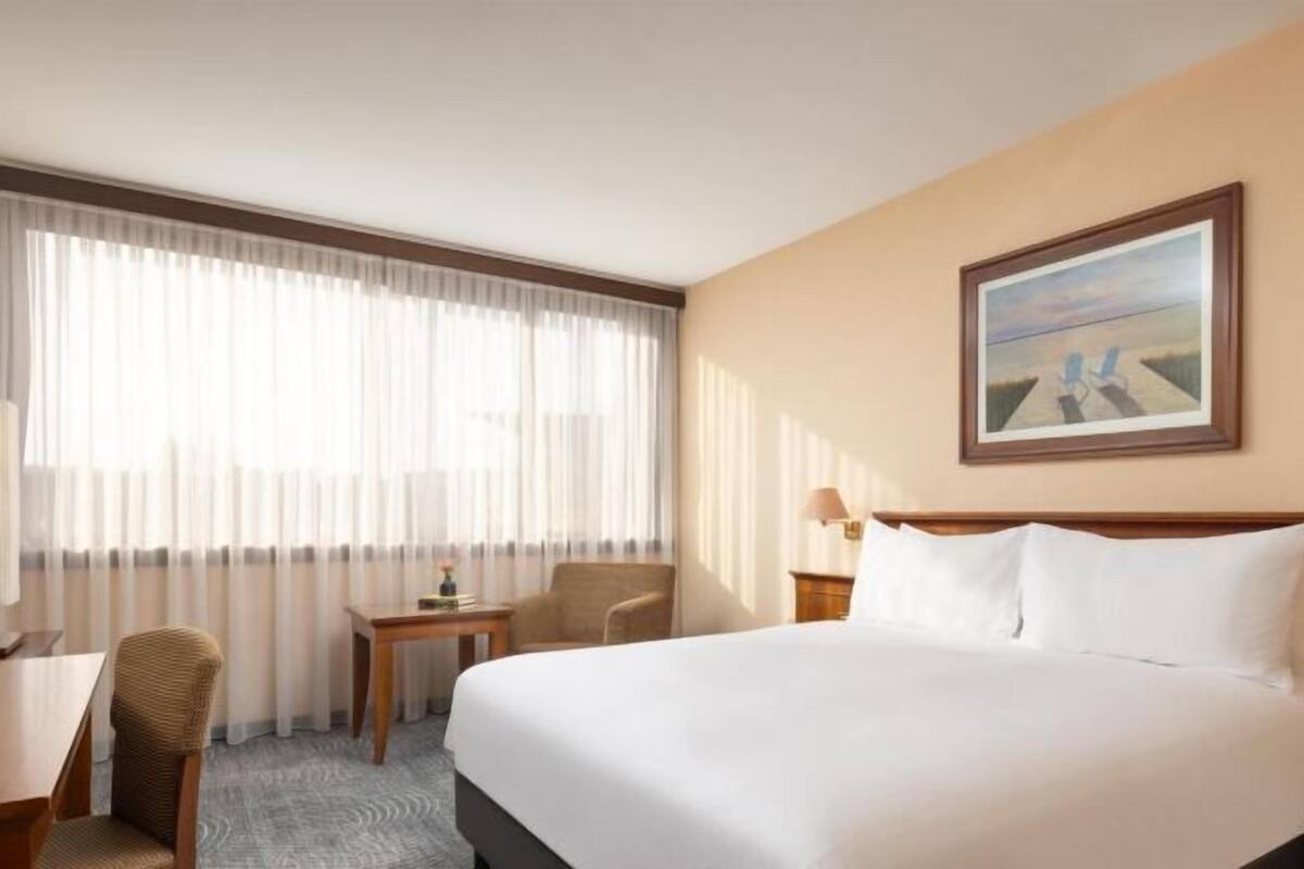 A hotel room with a large bed, a desk, a chair, a small table, and a painting on the wall.