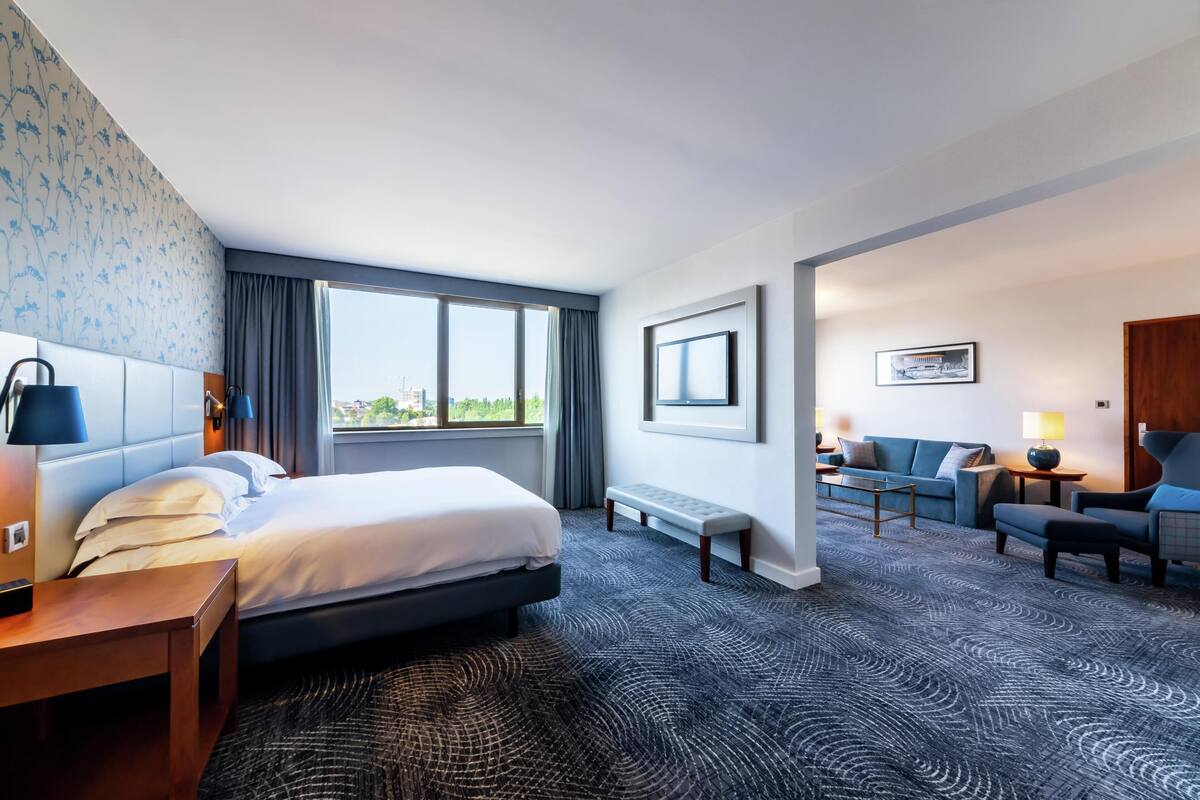 A hotel room with a bed, a desk, a sofa, a bench, and a TV.