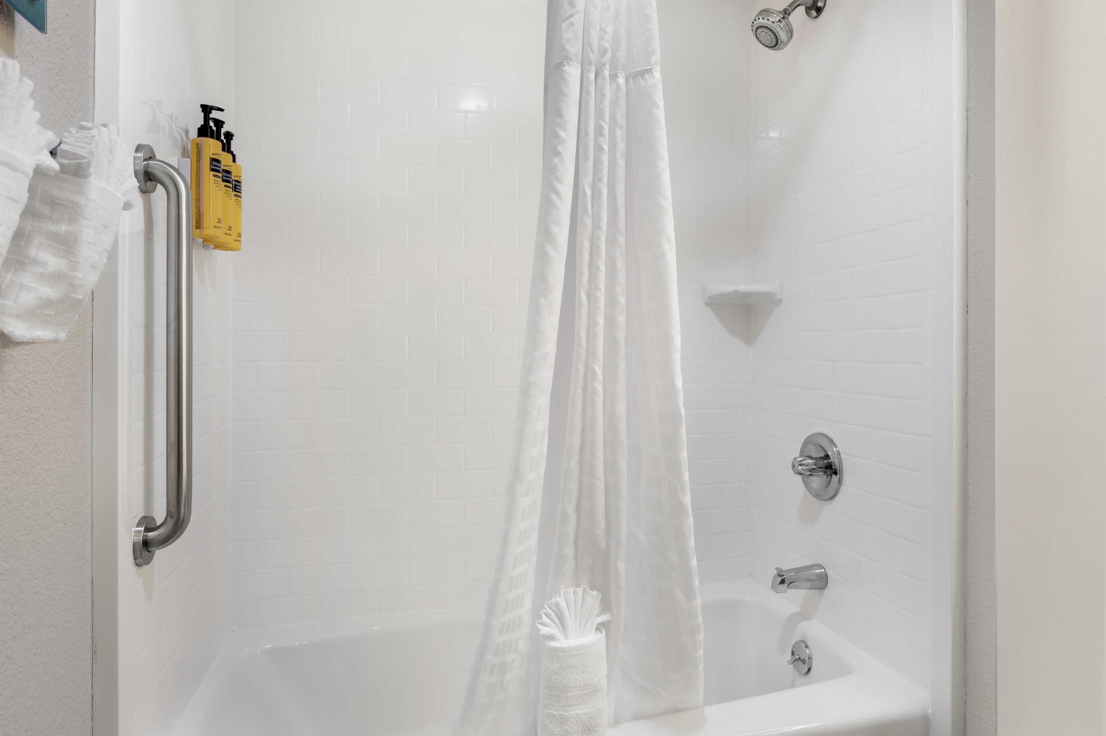 En bruser med hvidt gardin, brusehoved i hånden, samt en gul shampoo flaske.