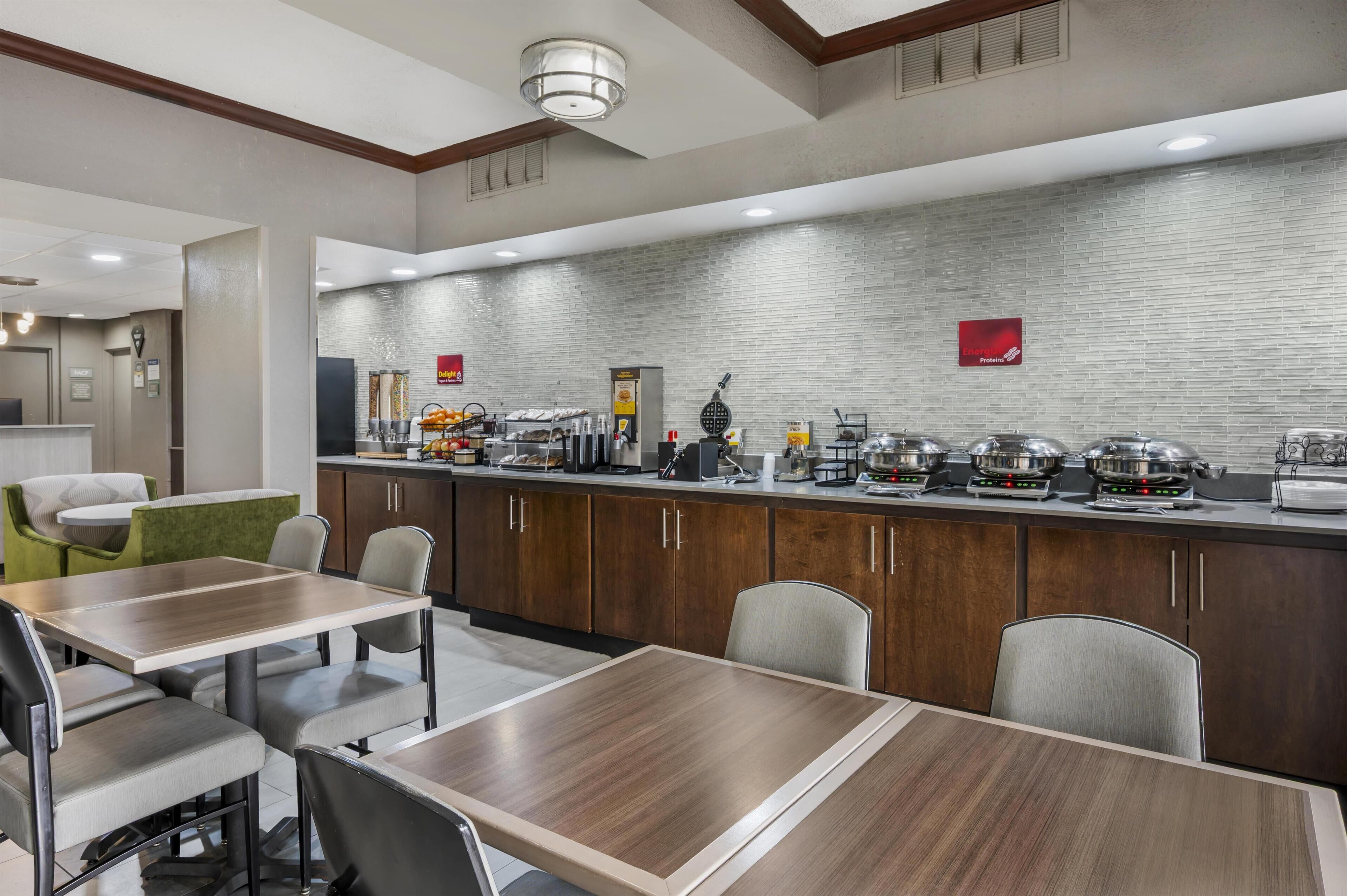 A modern hotel dining area with a brick backsplash, buffet setup, and seating arrangements.
