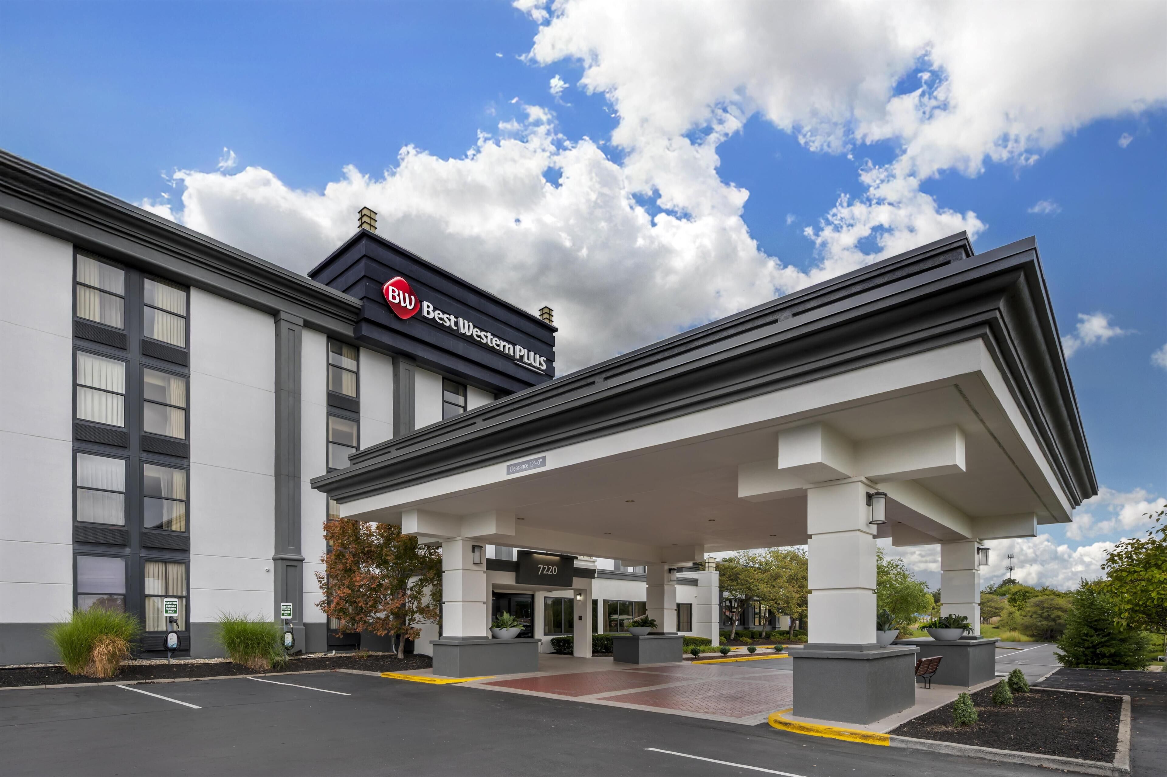 A hotel with a covered entrance, a sign reading "Blu Best Western Plus," and a parking lot.