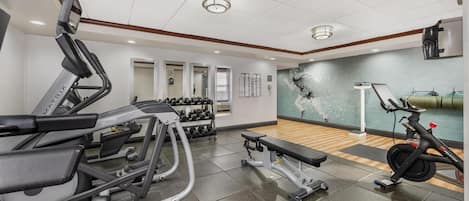 A gym with cardio equipment, dumbbells, and a wall-mounted exercise bike.