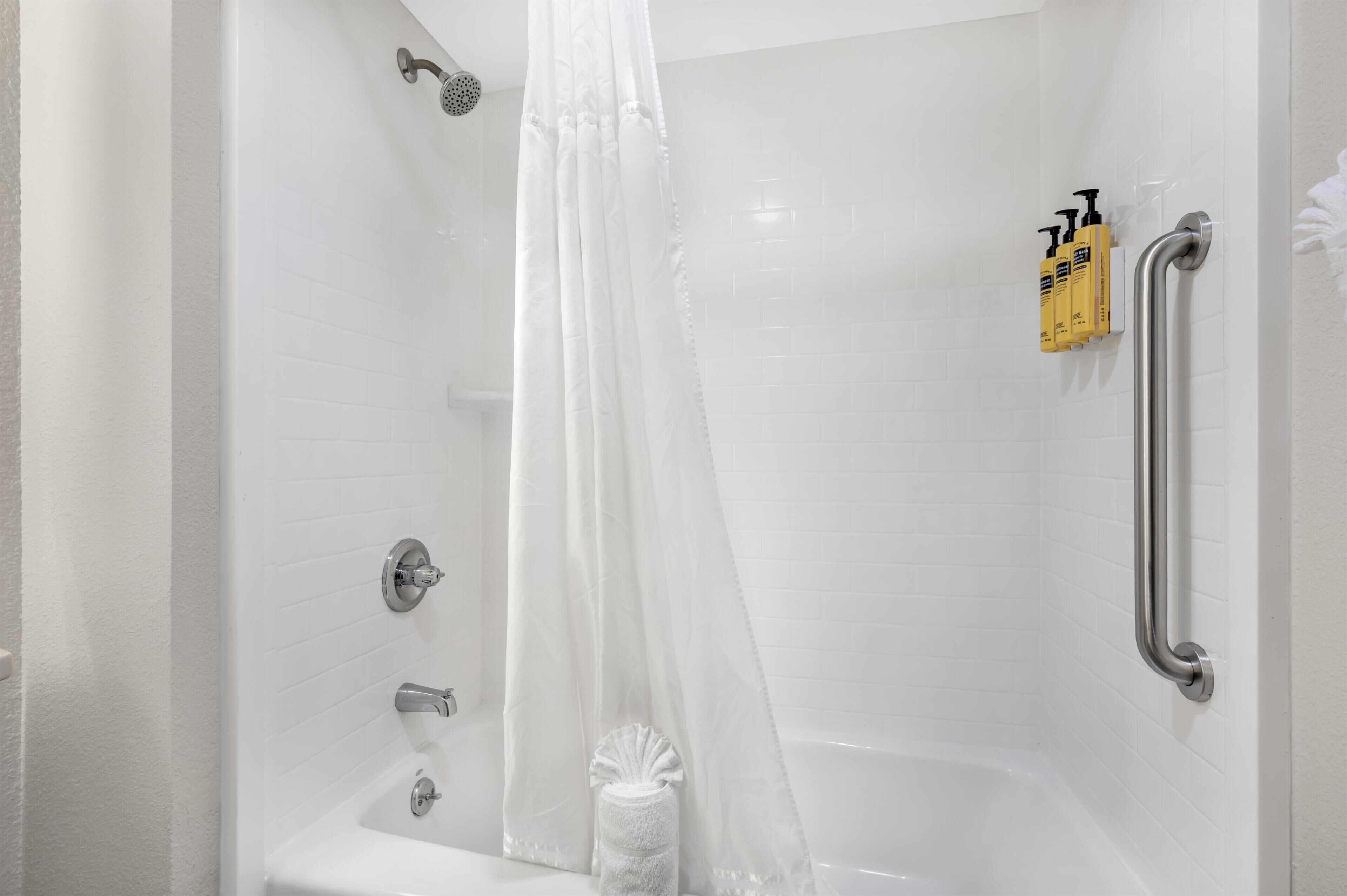 A shower with a white curtain, a handheld showerhead, a handheld massage nozzle, and a grab bar.