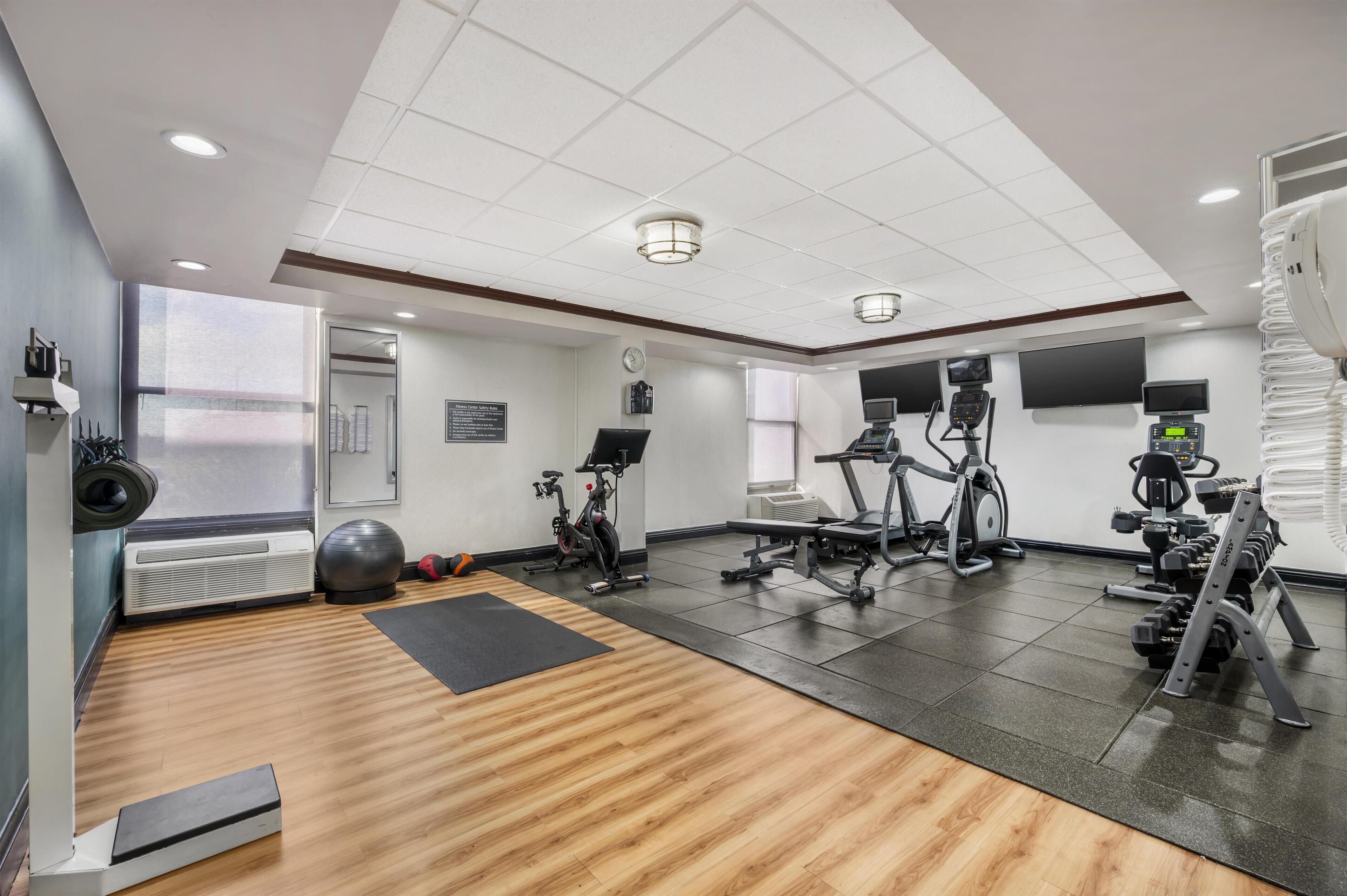 Un gimnasio con equipo de ejercicio, un espejo grande y suelo de madera.