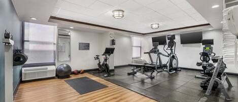 Une salle de sport équipée de matériel d’exercice, dotée d’un murmiroir et d’un plancher en bois.