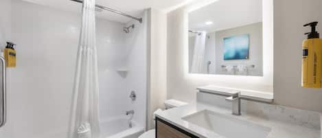 Une salle de bain moderne équipée d’une baignoire, de toilettes et d’un lavabo, avec un grand miroir et un rideau de douche.