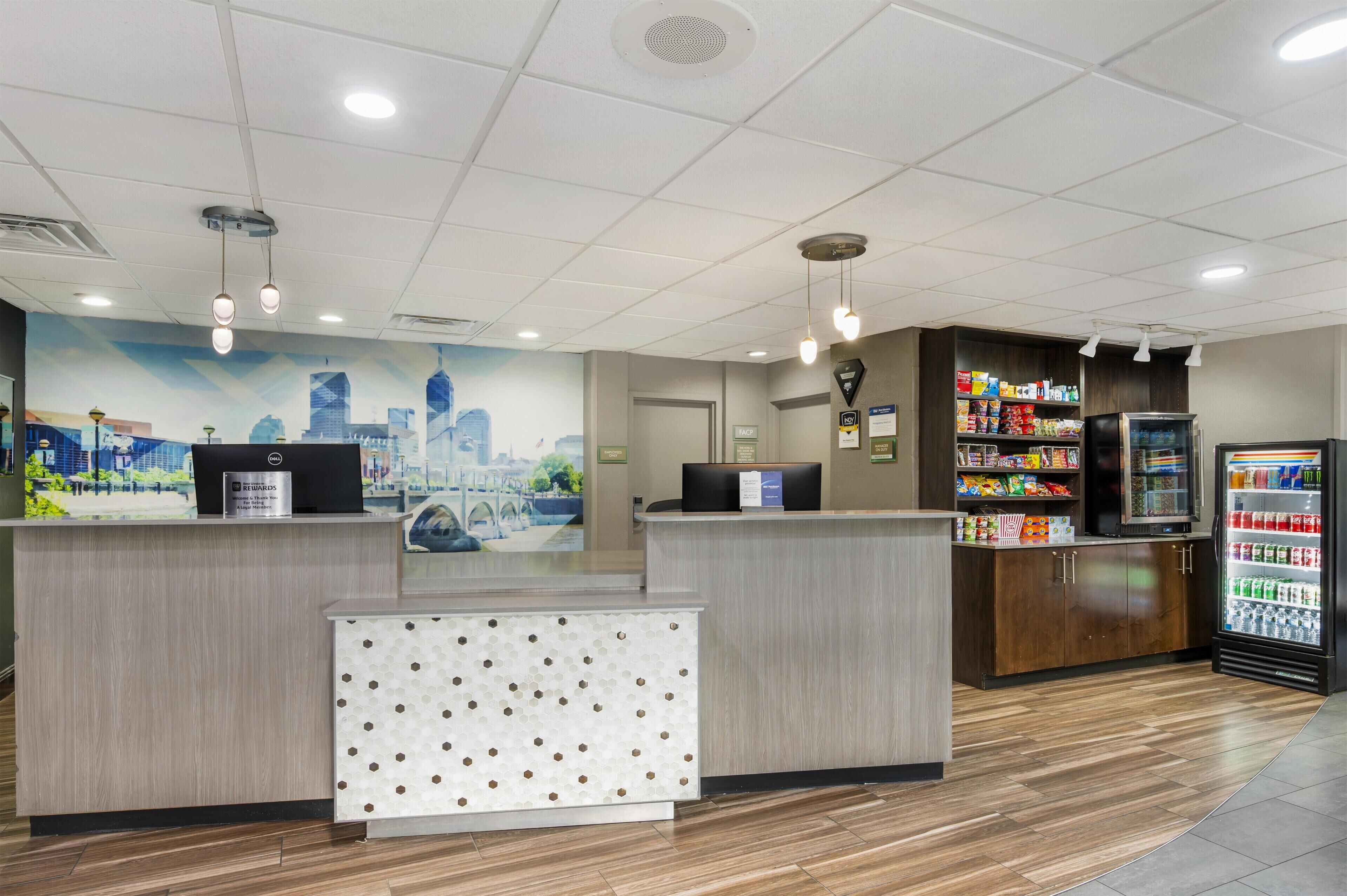 A reception area with a cityscape mural, a reception desk, a refrigerator stocked with beverages, and a patterned wall panel.