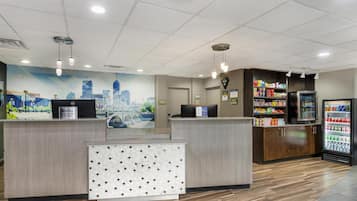 A reception area with a cityscape mural, a reception desk, a refrigerator stocked with beverages, and a patterned wall panel.