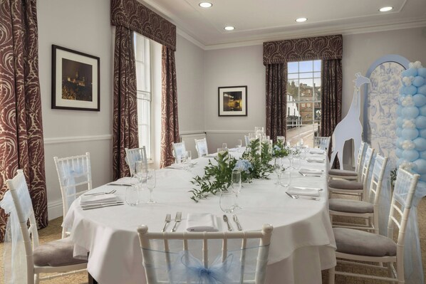 A formal dining room with a long table set for a meal, white chairs, and a decorative giraffe balloon arrangement.