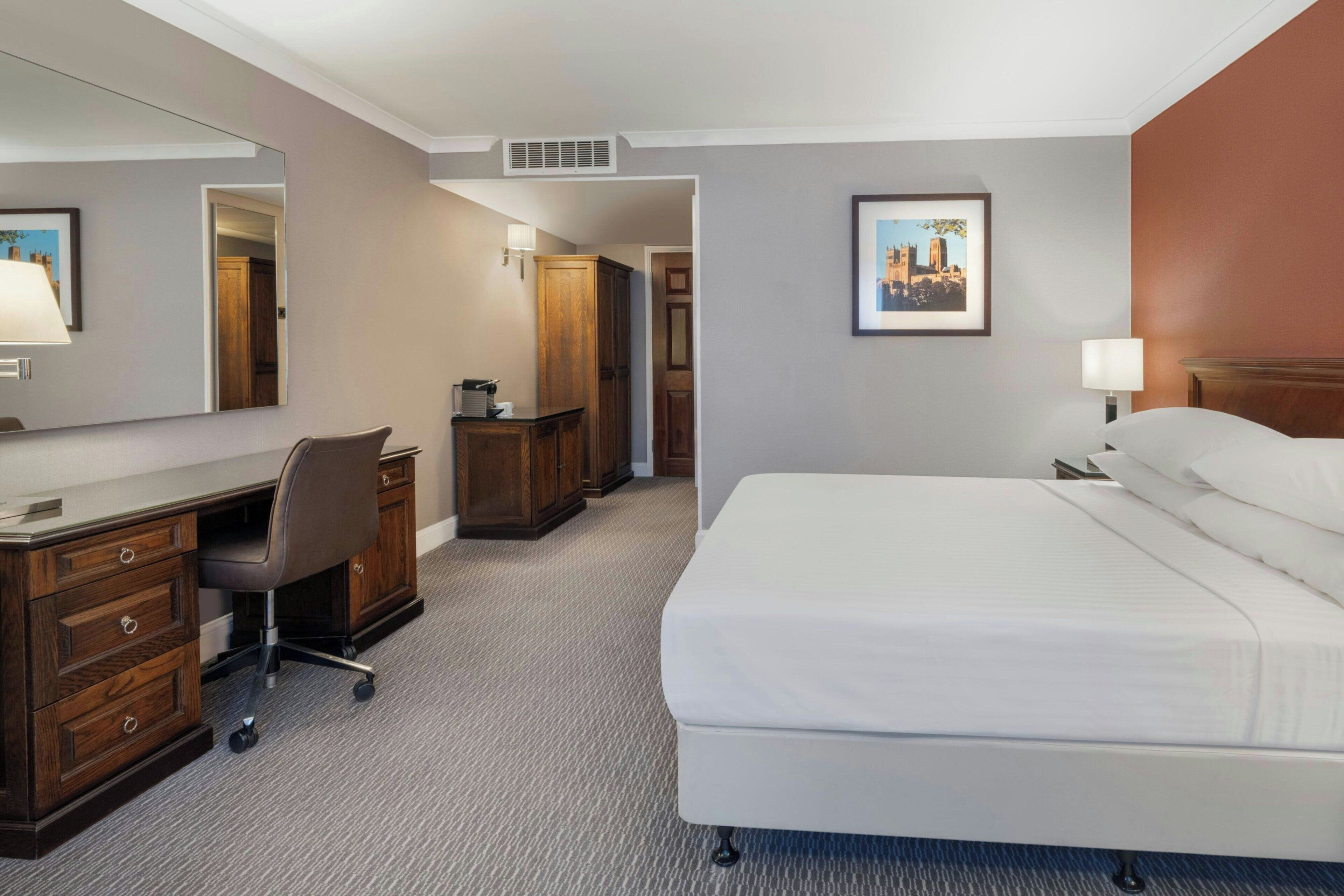 A hotel room with a bed, desk, chair, wardrobe, and a large mirror.