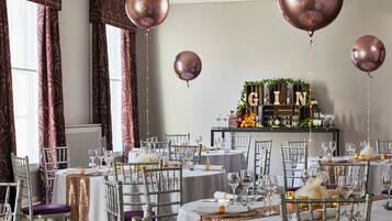 A banquet hall with round tables set for a formal event, featuring metallic chairs, white tablecloths, and a central floral arrangement.