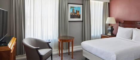Habitación de hotel con cama, escritorio, silla, mesita y lámpara.