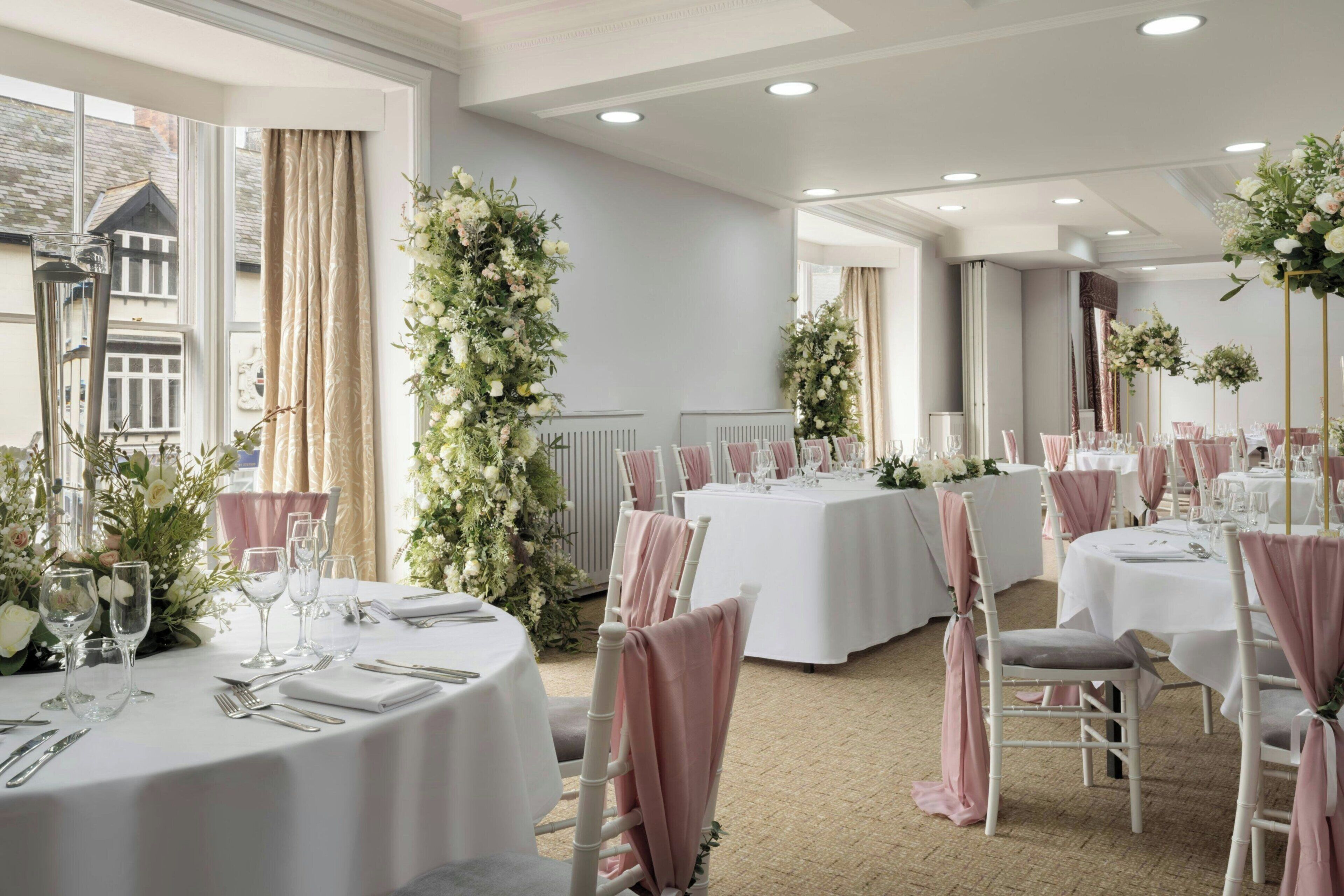 A formal dining room with round tables, white tablecloths, and pink chair covers.