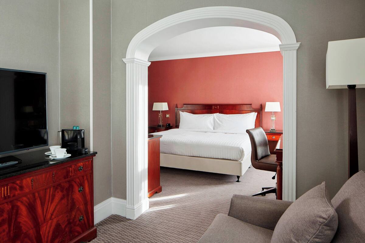 Habitación de hotel con una televisión de pantalla plana grande, una cama con ropa blanca, un aparador de madera y una zona de estar con sofá.