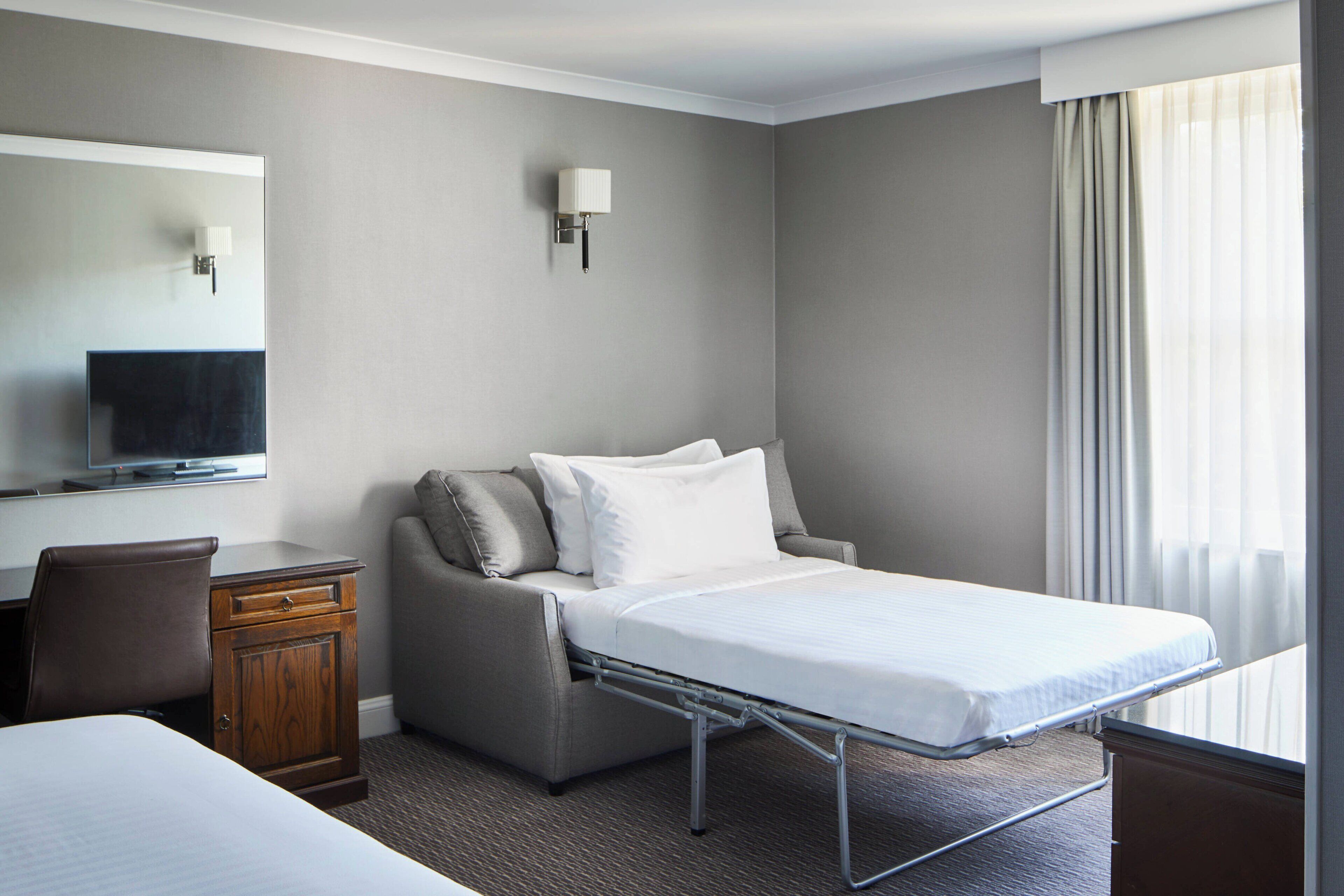 Habitación de hotel con cama, sofá, escritorio, televisor y ventana con cortinas.