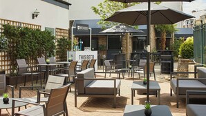 An outdoor patio area with tables and chairs, a sign reading "THIS BEER", and a building with a sign that says "BREWDOG".