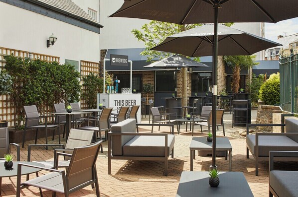 An outdoor patio area with tables and chairs, a sign reading "THIS BEER", and a building with a sign that says "BREWDOG".