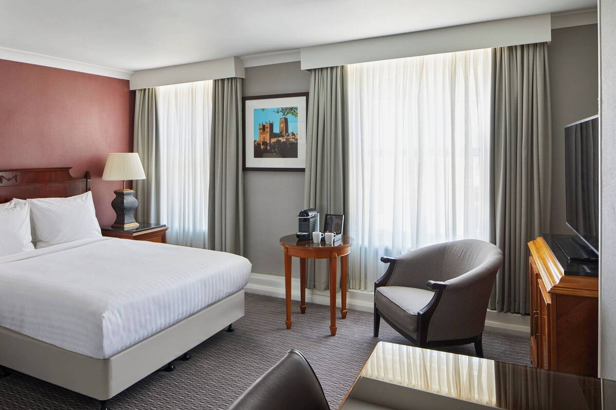 Habitación de hotel con una cama grande, una silla, una mesita, un televisor y un cuadro en la pared.