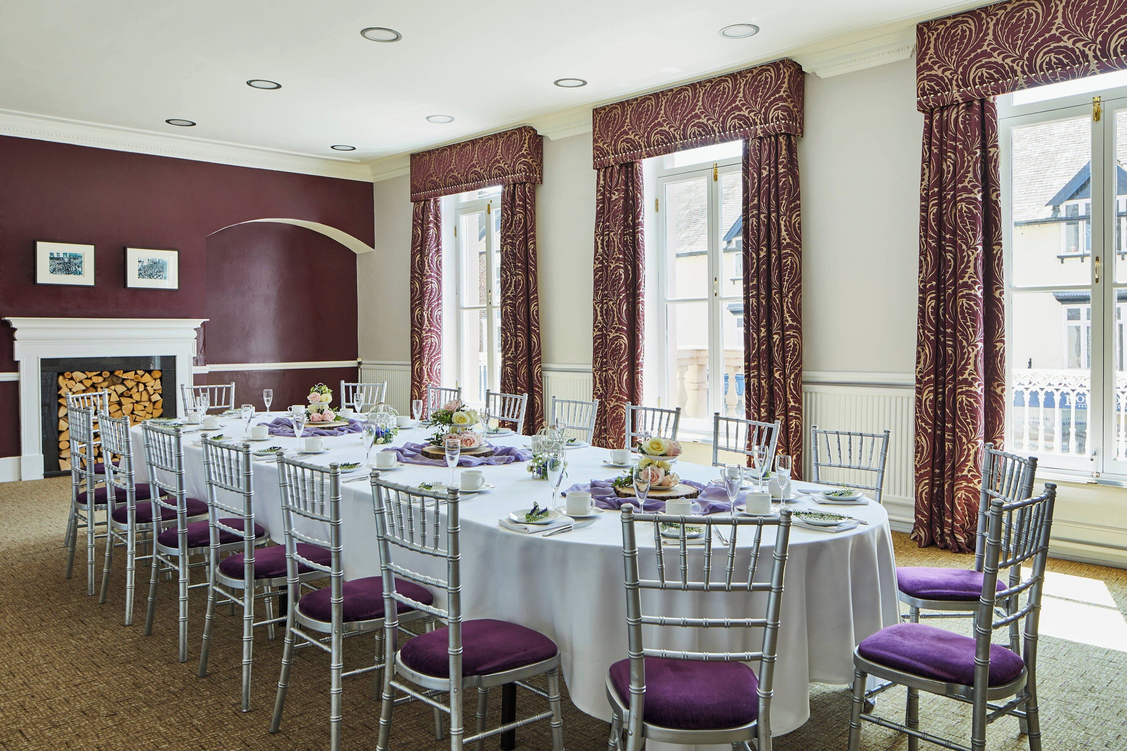 A formal dining room with round tables, silver chairs, and purple cushions.