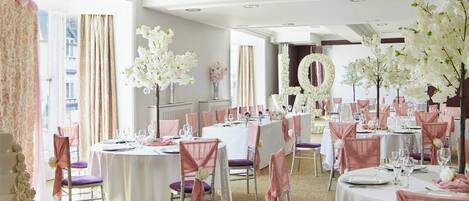 A banquet hall with round tables, chairs, and floral decorations.
