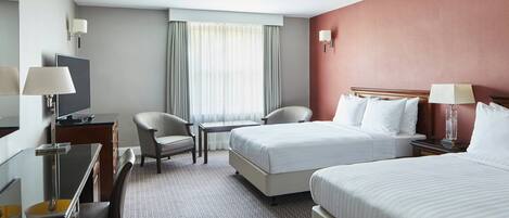 A hotel room with two beds, a desk with a chair, a TV, and a window with curtains.