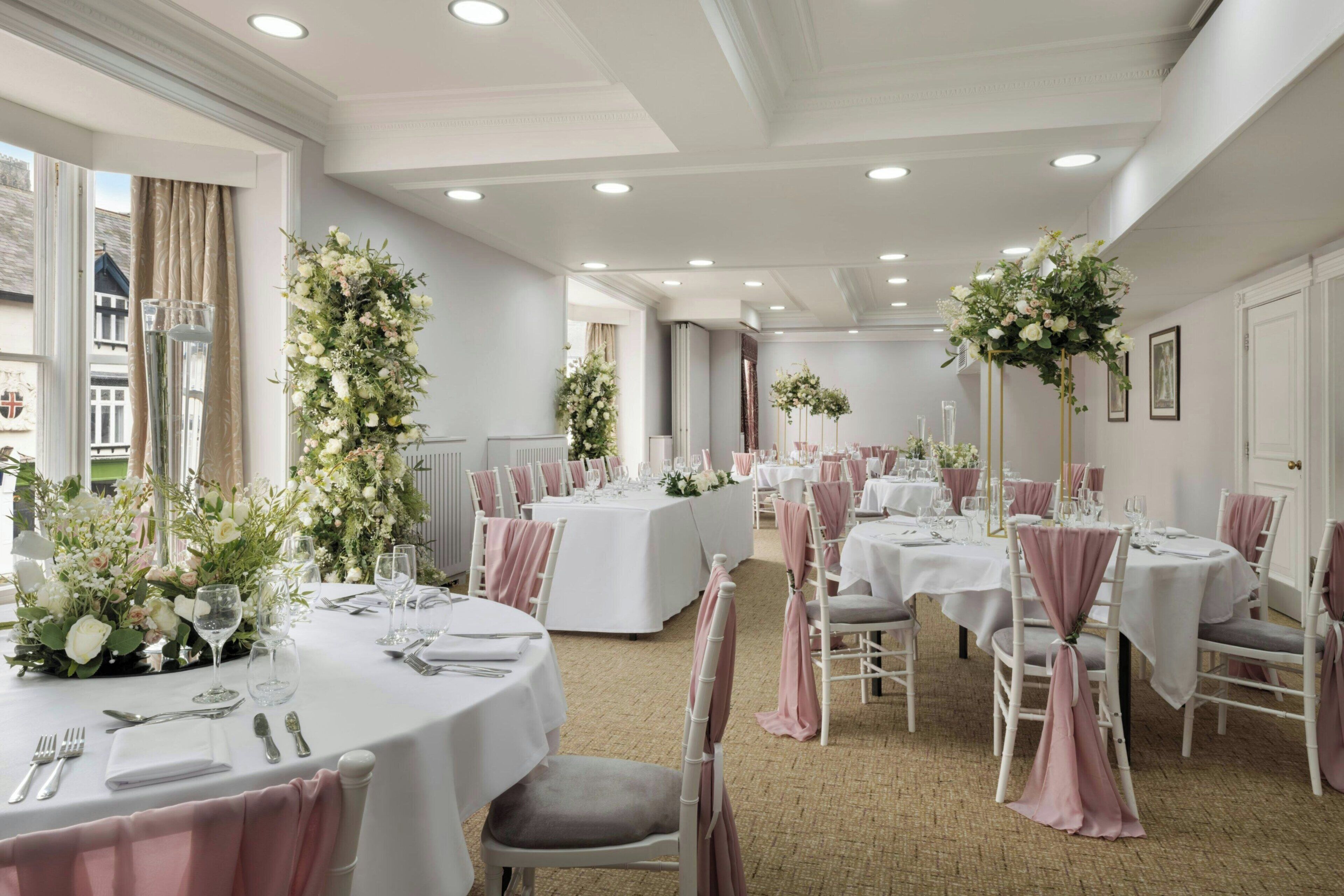 A banquet hall with round tables, white tablecloths, and pink chair covers.