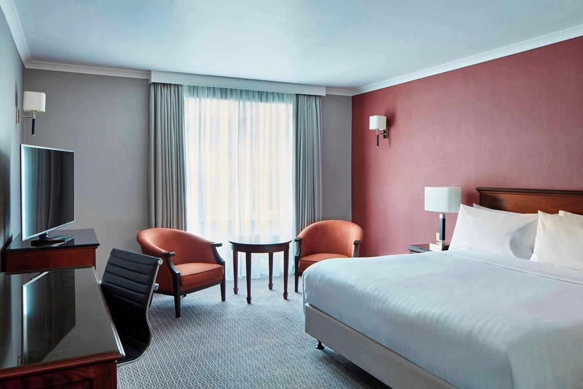 Habitación de hotel con cama, dos sillones, una mesita, escritorio con televisor y lámpara.