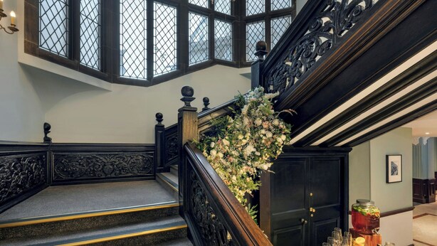 Una imponente escalera con barandillas ornamentales y un arreglo floral, que conduce a una puerta.